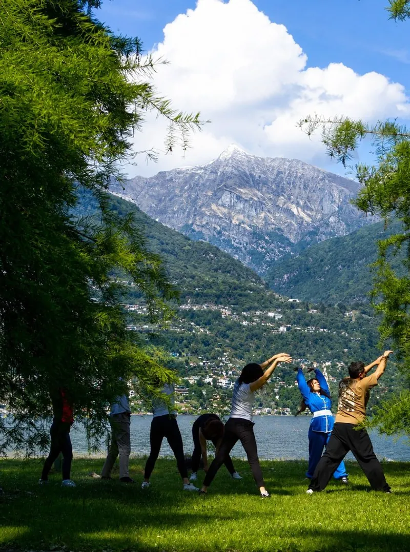 Gruppo che pratica Qi Gong sul prato davanti al lago e alla montagna